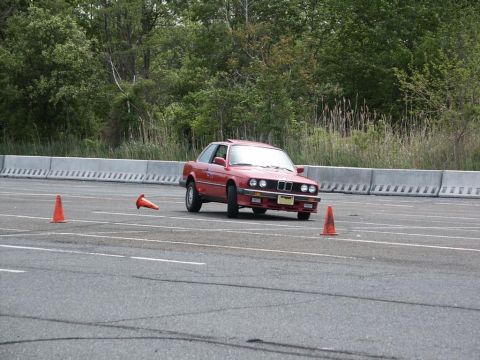 2001 Mercury Grand Marquis - A red BMW E30 coupe navigates a course marked by orange traffic cones on a sunny day.
