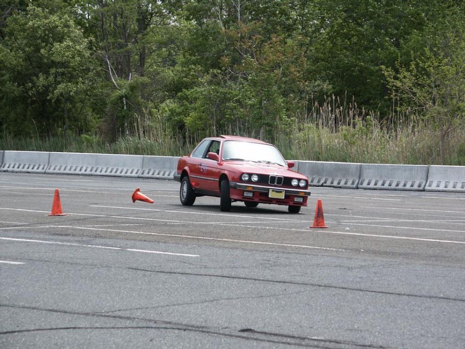 red BMW E30 coupe driving around orange cones on a paved course