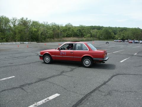 2001 Mercury Grand Marquis - A red BMW E30 coupe with racing number 241 participates in an autocross event, with other cars visible in the background.