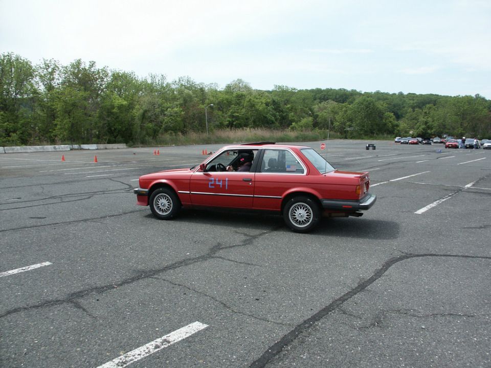 Red BMW E30 coupe with racing number 241 on its side, seen from the side at an autocross event