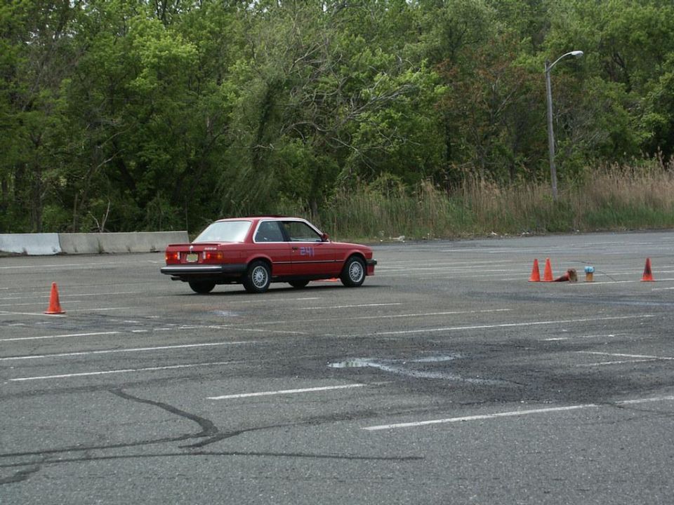 Red coupe with number 241 on door, driving on asphalt with orange cones