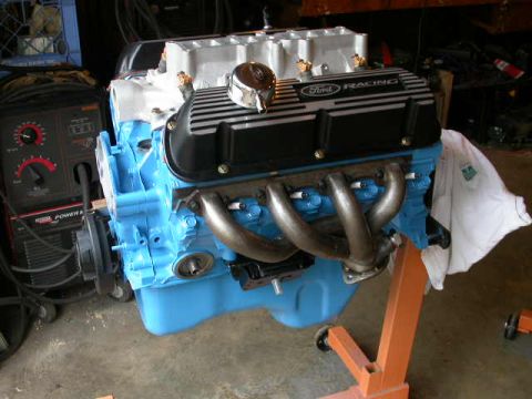 1990 Ford Bronco - A blue Ford Racing engine is mounted on an orange stand, with a welding machine visible to the left.