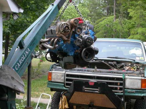 1990 Ford Bronco - An engine is being hoisted out of a green truck using a mechanical crane.