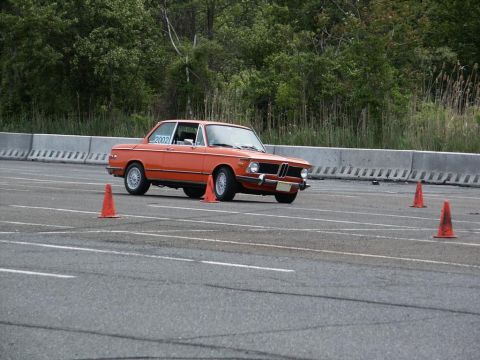 2001 Mercury Grand Marquis - An orange BMW 2002 navigates a course marked by traffic cones on a sunny day.