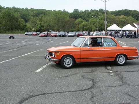 2001 Mercury Grand Marquis - An orange BMW 2002 is seen on the track at an autocross event, with other cars parked in the background.