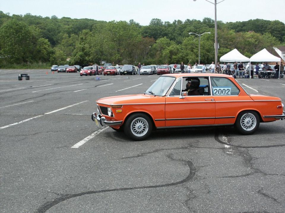 Orange BMW 2002 with '2002' decal on side window, seen at autocross event