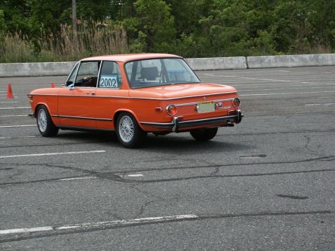 2001 Mercury Grand Marquis - An orange BMW 2002 is parked on an asphalt surface, possibly at a track event.