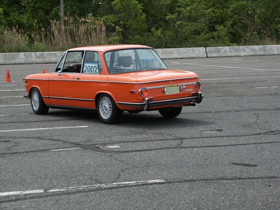 orange BMW 2002 on asphalt with trees and concrete barrier in background