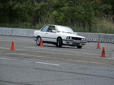 2001 Mercury Grand Marquis - A white BMW E30 coupe is seen maneuvering through an autocross course with orange cones on the track.