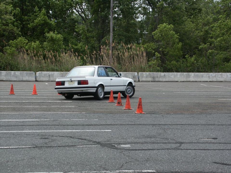 White BMW E30 coupe navigating an autocross course with orange cones