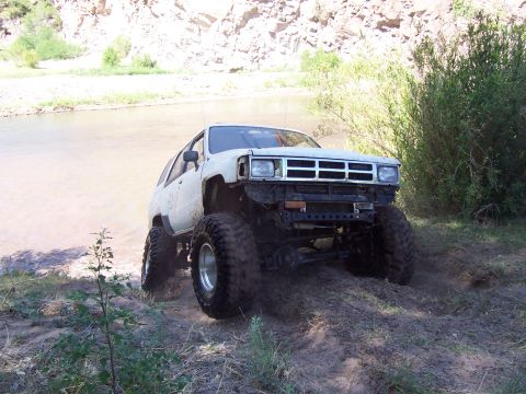 1981 Ford F-150 - Modified SUV with large tires navigates a dirt trail next to a body of water.