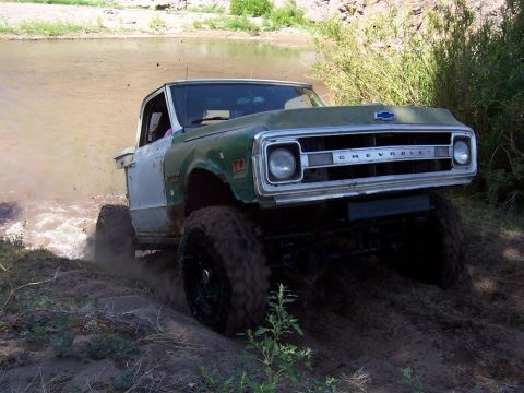 1981 Ford F-150 - Modified Chevrolet pickup truck navigates a muddy off-road course near a river.
