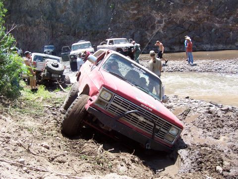 1981 Ford F-150 - Several off-road vehicles navigate a muddy terrain near a river.