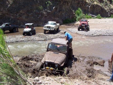 1981 Ford F-150 - Several off-road vehicles navigate a muddy riverbed, with one Jeep deeply stuck in the mud.