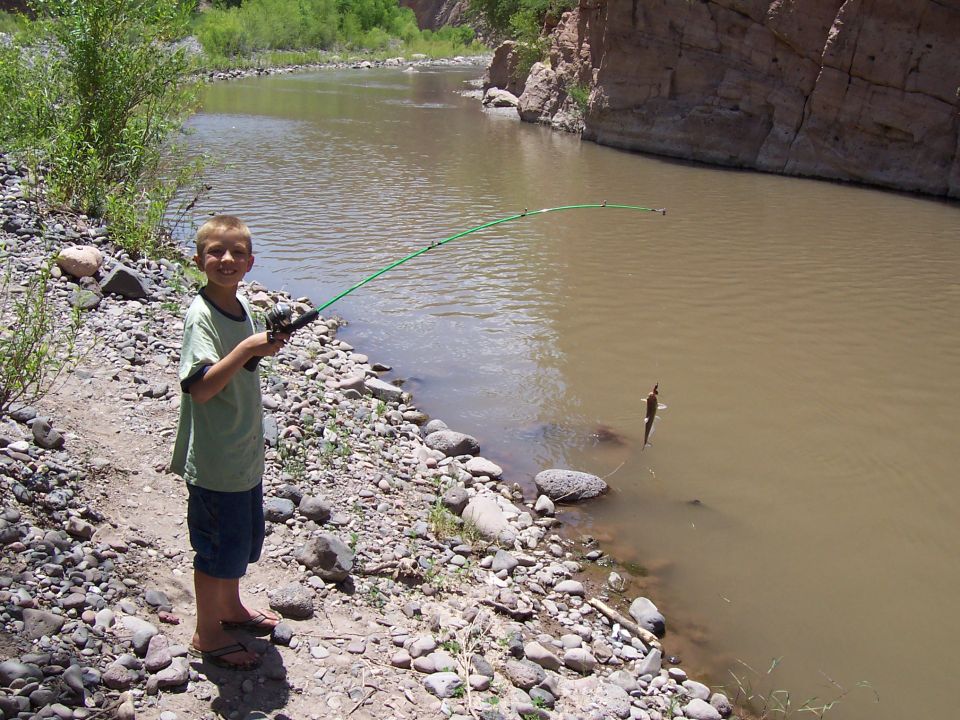 Boy with fishing rod on rocky shore of muddy river