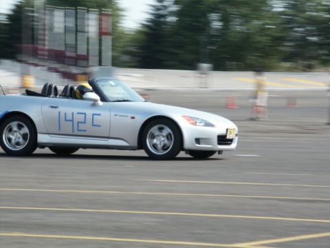 2001 Mercury Grand Marquis - A silver convertible sports car, identified by the blue racing numbers '142C', navigates a race track during an event.