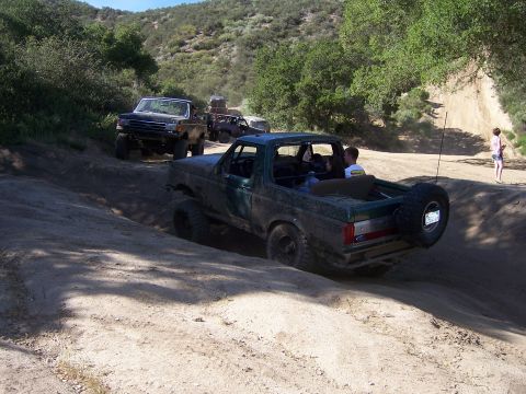 1991 Ford Bronco - Several off-road vehicles, including a 1991 Ford Bronco, navigate a dusty trail.