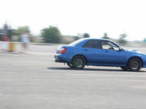 2001 Mercury Grand Marquis - A blue sedan, possibly a Subaru WRX, is captured in motion on a race track with motion blur indicating speed.