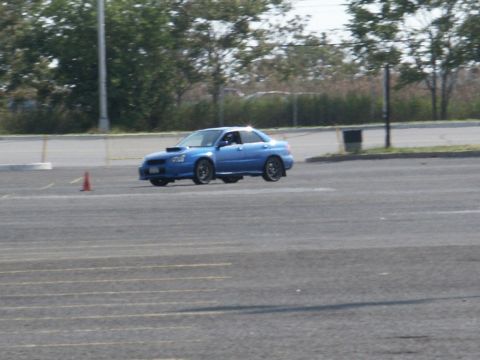 2001 Mercury Grand Marquis - A blue Subaru WRX STI sedan is captured mid-air during a motorsports event on an asphalt course.