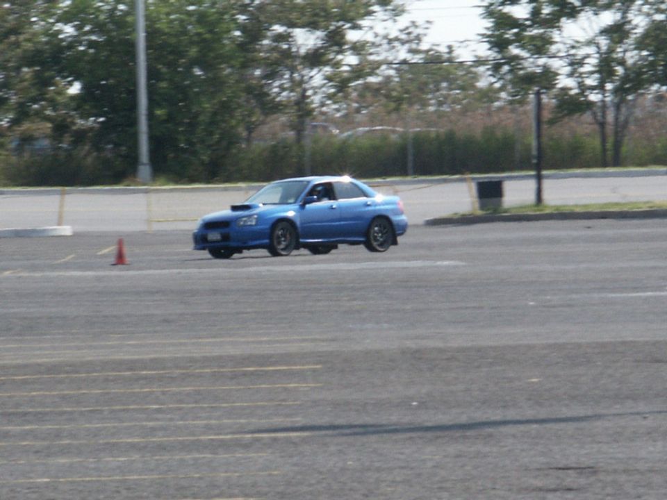 Blue Subaru WRX STI sedan with hood scoop, front-wheel lifted, on asphalt course