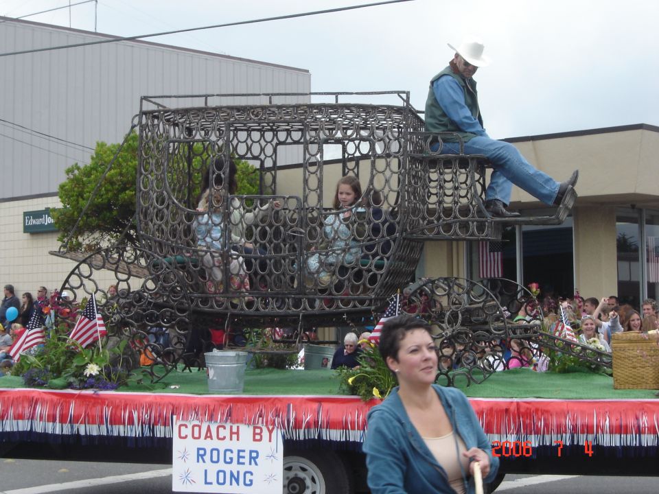 Parade float with a carriage made of horseshoes, carrying people. Sign says 'COACH BY ROGER LONG'