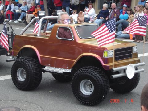 1993 Ford Bronco - A small, custom-built vehicle with large tires participates in a parade, adorned with American flags.