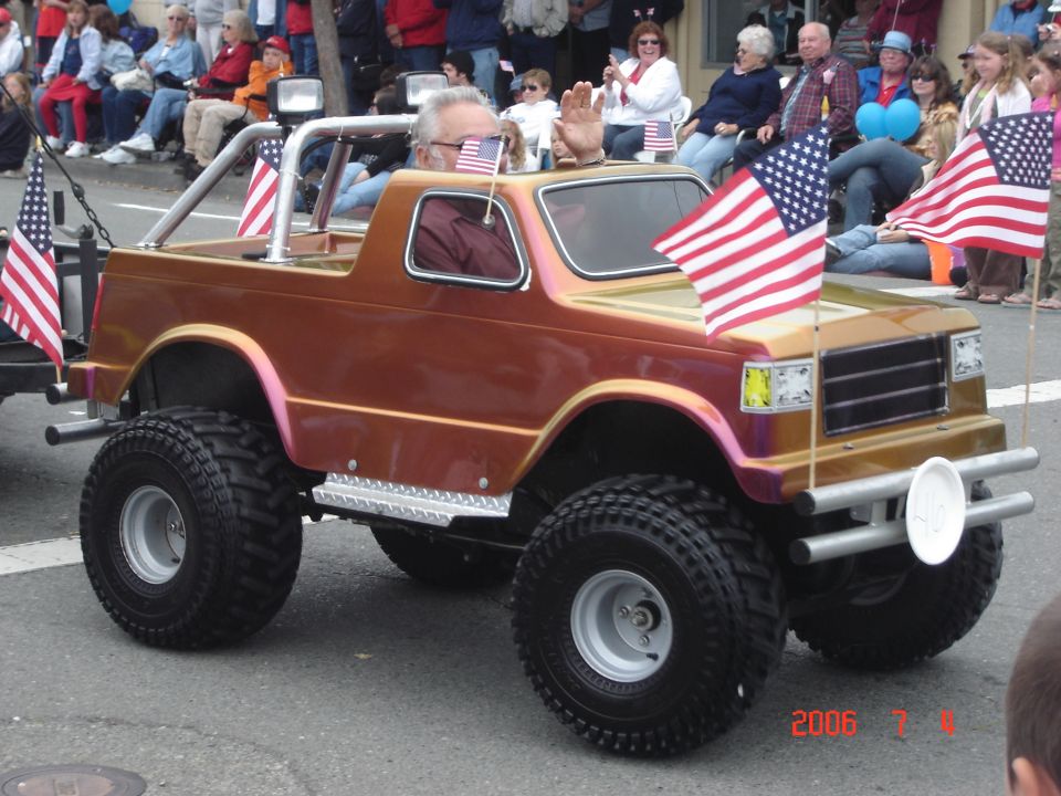 Miniature off-road vehicle with American flags, driven by an older man waving