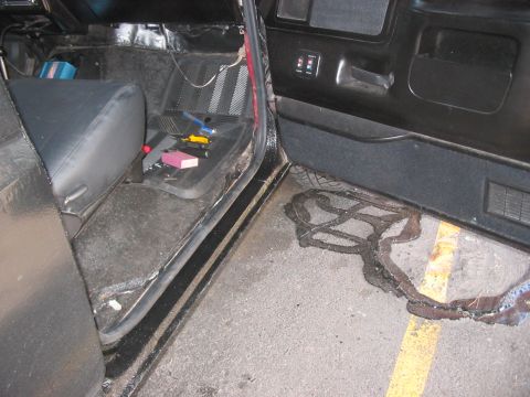 1991 Ford Bronco - The interior of a vehicle shows tools on the floor mat, with a dark liquid spill visible outside the open door.