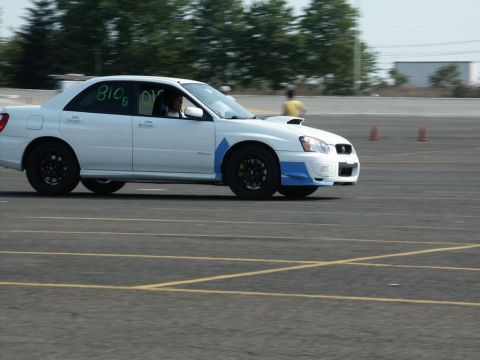 2001 Mercury Grand Marquis - A white Subaru Impreza WRX STI sedan with racing numbers '810B' on the window navigates a track with orange cones visible.