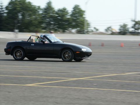 2001 Mercury Grand Marquis - A black convertible sports car navigates a track, with a driver visible in a helmet.
