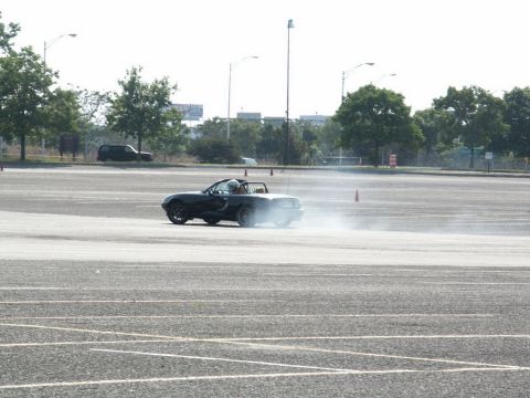 2001 Mercury Grand Marquis - A black convertible Mazda Miata is seen drifting in an open lot, creating a cloud of smoke.