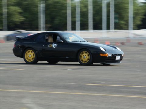 2001 Mercury Grand Marquis - A black coupe with distinctive yellow wheels navigates a race track, with another vehicle blurred in the background.