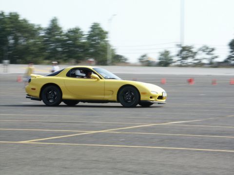 2001 Mercury Grand Marquis - A yellow Mazda RX-7 navigates a course on a sunny day, with a driver wearing a helmet visible inside.