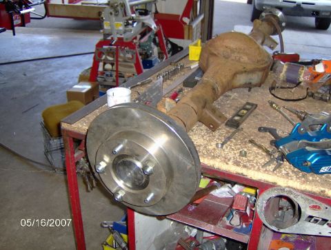1978 Ford Bronco - Rear axle assembly with disc brake rotor and caliper bracket on a workbench, with tools and shop equipment in the background.