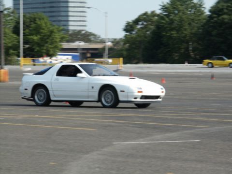 2001 Mercury Grand Marquis - A white sports coupe navigates an asphalt course marked with orange cones, with a yellow car visible in the distance.