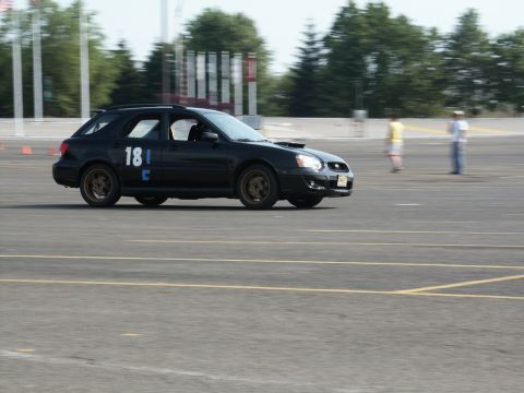 2001 Mercury Grand Marquis - A black Subaru Impreza WRX wagon is seen on a race track with blurred background figures.