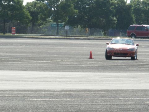 2001 Mercury Grand Marquis - A red convertible sports car navigates a course marked by an orange cone, with a red SUV visible in the distance.