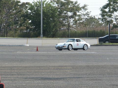 2001 Mercury Grand Marquis - A white Porsche 911 with racing number 21 participates in an event on a paved lot, with another vehicle visible in the background.