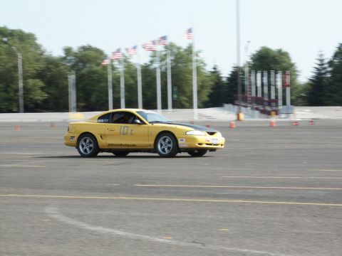 2001 Mercury Grand Marquis - A yellow 1996 Ford Mustang Cobra participates in a motorsports event, displaying racing numbers on its side.