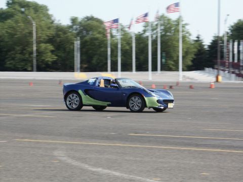 2001 Mercury Grand Marquis - A blue Lotus Elise with contrasting green body panels navigates a course marked by orange cones, with American flags flying in the distance.