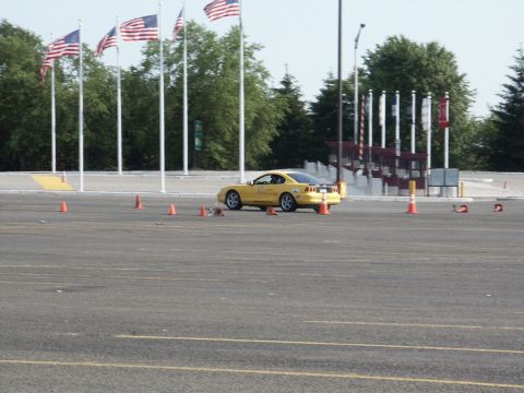 2001 Mercury Grand Marquis - A yellow sports car navigates a course marked by orange cones, with American flags flying in the background.