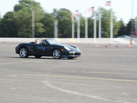 2001 Mercury Grand Marquis - A black Porsche Boxster is seen on a race track with orange cones and American flags in the background.