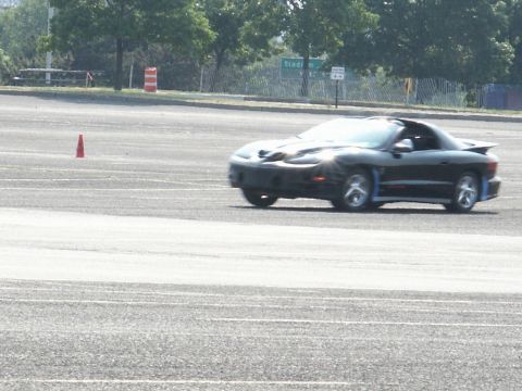 2001 Mercury Grand Marquis - A black Pontiac Firebird Trans Am is seen in motion on a paved surface, with traffic cones visible in the background.