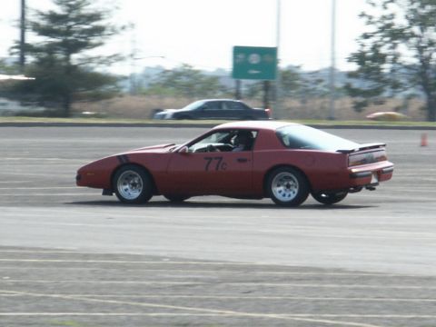 2001 Mercury Grand Marquis - A red Pontiac Firebird with racing stripes and the number 77c on its door is seen on a track, with another vehicle in the background.