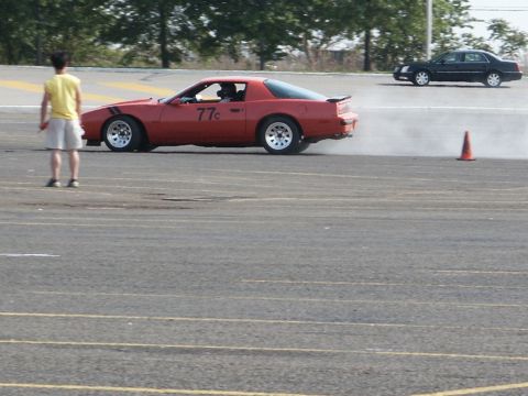 2001 Mercury Grand Marquis - A red sports car with racing stripes and the number 77c on its door drifts on a paved surface, with a black sedan in the background.