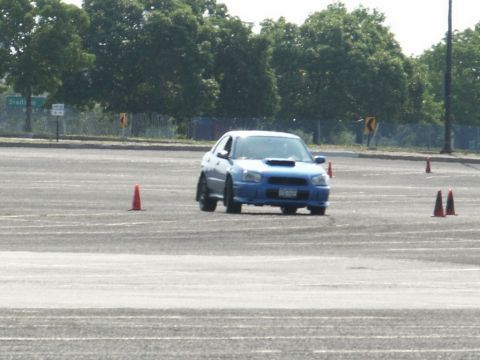 2001 Mercury Grand Marquis - Blue Subaru Impreza WRX STI navigates a cone course on a sunny day.