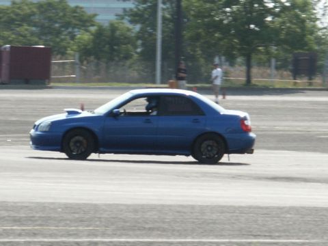 2001 Mercury Grand Marquis - A blue sedan with a hood scoop is seen from the side on a paved track.