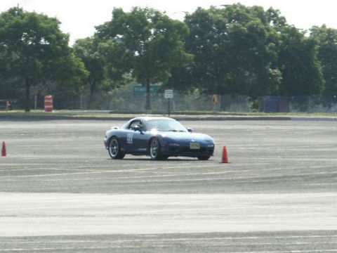 2001 Mercury Grand Marquis - A blue Mazda RX-7 navigates a course marked by orange cones on a paved surface.