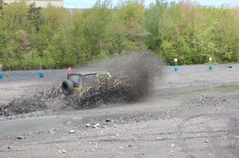 1991 Ford Bronco - A yellow Jeep Wrangler navigates a muddy obstacle, sending dirt and debris flying.