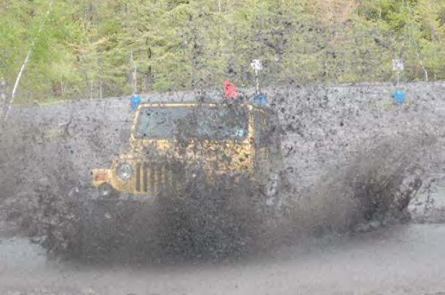 Yellow Jeep splashing through mud, front view